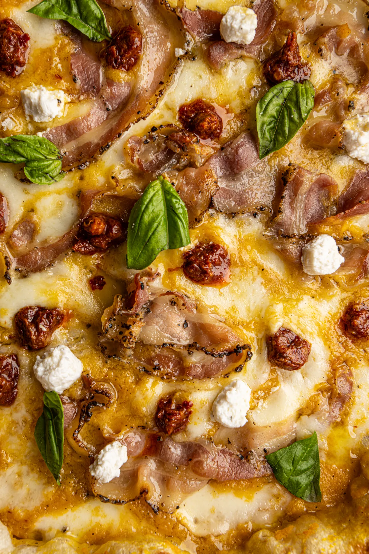 Primo piano della pizza: pancetta pepata, ciuffi di ricotta, pomodori secchi e basilico