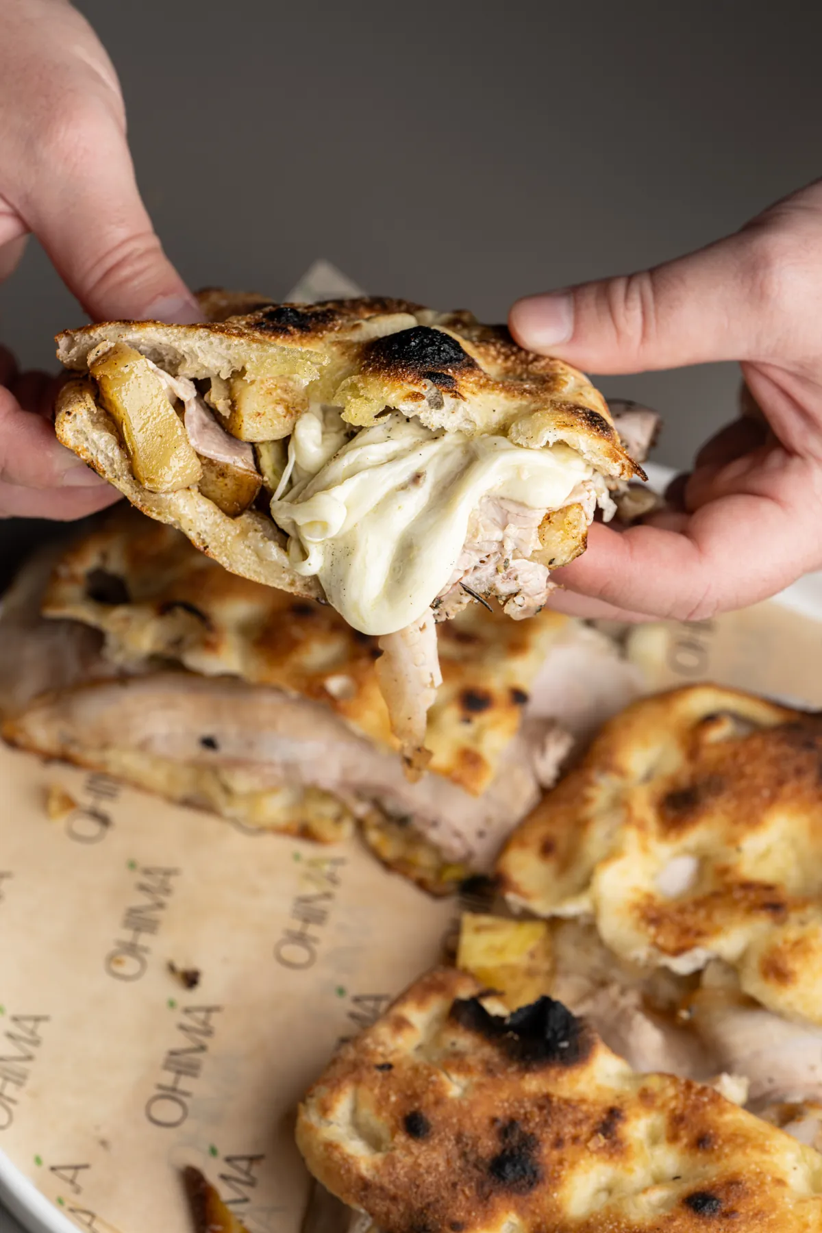Due mani aprono una pizza ripiena: formaggio filante, carne arrosto e patate dentro l'impasto dorato e bruciacchiato